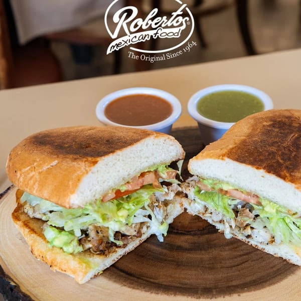 A Roberto's Mexican Food torta, cut in half, with two small bowls of salsa.