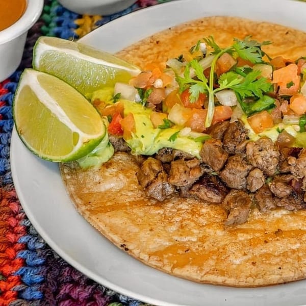 A carne asada taco from Roberto's Mexican Food, topped with guacamole, pico de gallo, and lime wedges.