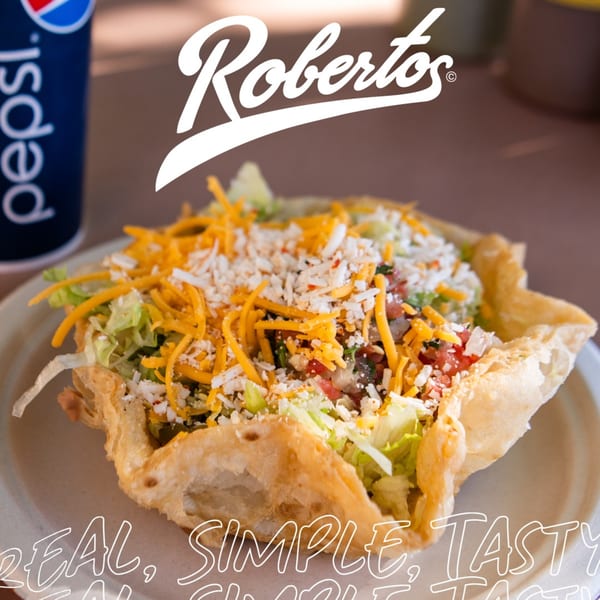 A Roberto's Mexican Food taco salad in a crispy shell, topped with cheese and lettuce, next to a Pepsi.